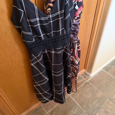Two sleeveless women's dresses hanging on a wooden door, including a black grid-patterned dress with a lace waist detail and a...