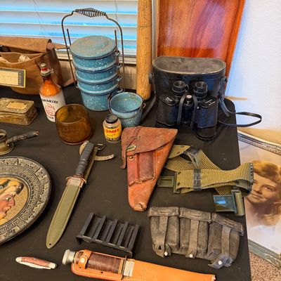 Collection of vintage military gear and collectibles, including combat knives, a leather holster, webbed belt, binoculars in case, and...