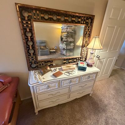 French Provincial style off-white double dresser with brass hardware, paired with a large ornate framed wall mirror and decorative table...