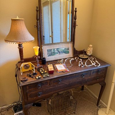 Vintage dark wood vanity desk with attached swivel mirror, set with tabletop lamps, costume jewelry, and decor.