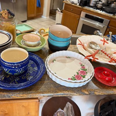Assortment of colorful ceramic kitchenware and serving dishes, including hand-painted plates, bowls, a fluted quiche dish with floral...