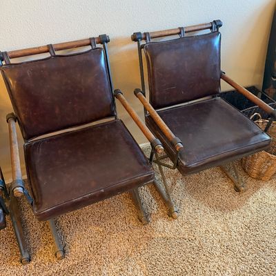 Pair of vintage campaign-style armchair folding chairs featuring dark brown leather-like vinyl upholstery, wooden dowel armrests, and...