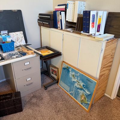 Home office workspace featuring a metal filing cabinet desk base, a plywood storage cabinet topped with three-ring binders, and a framed...