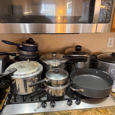 Assorted cookware collection including aluminum pressure cookers, stainless steel saucepans with lids, blue non-stick pots, and a large...