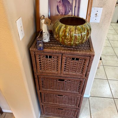 Brown woven wicker storage chest with five drawers, topped with decorative items including a glazed ceramic bowl and framed photo.
