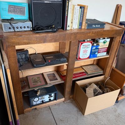 Wooden shelving unit holding various vintage electronics, books, framed art, and workshop supplies including an Optimus amplifier and...