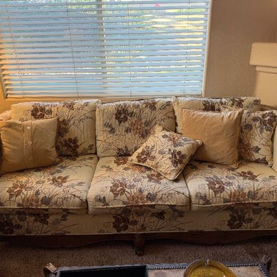 Traditional three-cushion sofa featuring a beige floral tapestry upholstery, dark carved wooden trim, and coordinating accent pillows.
