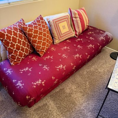Armless futon couch with a patterned magenta cover and an assortment of decorative accent pillows.
