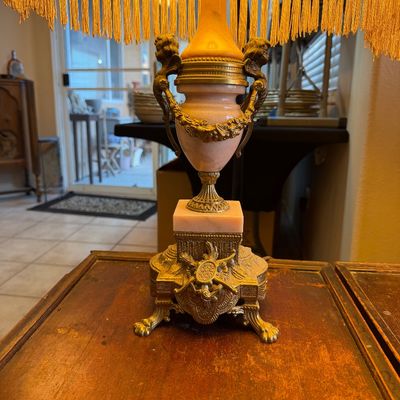 Vintage Neoclassical table lamp featuring a pink alabaster urn body, ornate brass mounts with lion-head handles, and a yellow...