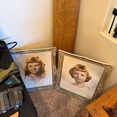 Pair of vintage framed hand-colored portrait prints of young girls in matching ornate silver-painted frames, leaning against a wall next...