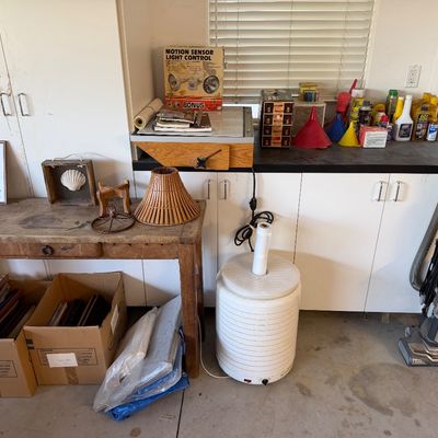 Workshop workbench and wooden console table featuring various household goods, including a Shark upright vacuum, food dehydrator, framed...