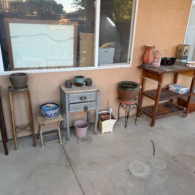 Collection of patio decor including plant stands, ceramic pots, small accent tables, and decorative lamps lined up against an exterior wall.
