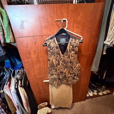 Vintage cherub print tapestry vest paired with tan trousers hanging on a wooden wardrobe.