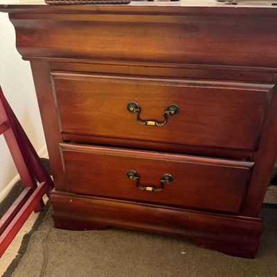 Traditional wooden nightstand featuring a rich cherry finish, two drawers with brass bail handles, and a molded crown top.