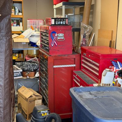 Workshop area filled with red metal rolling tool chests, a Shop-Vac wet/dry vacuum, plastic storage totes, and miscellaneous household...
