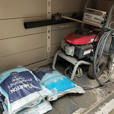 Sale Photo Thumbnail #123: PowerWasher 2600 PSI 2.3 GPM gas-powered pressure washer with a Honda engine, spray wand, and hose, alongside bags of Morton Professional's Choice pool salt stored in a shed.