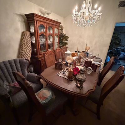 Traditional dining room set with cane-back chairs, a matching china hutch, a crystal chandelier, and an upholstered accent armchair.