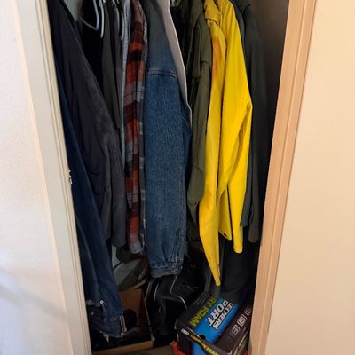 Closet filled with men's vintage and contemporary outerwear, including a bright yellow raincoat, denim jacket, flannel shirts, and...