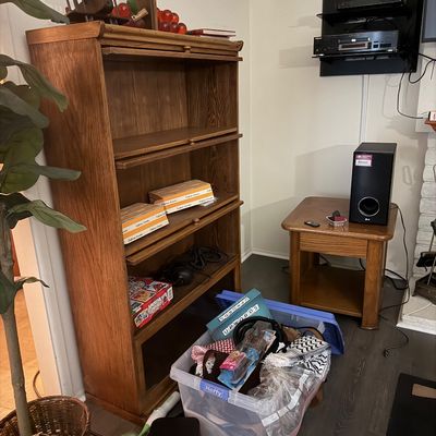 Oak barrister-style bookcase featuring roll-up doors, shown alongside a matching wooden side table, electronics, and household goods.