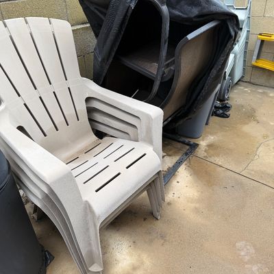 Stack of beige plastic Adirondack-style patio chairs sitting alongside covered outdoor furniture.