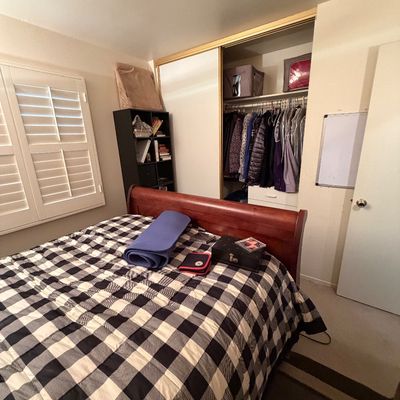 Wooden sleigh bed frame with black and white buffalo plaid comforter in a bedroom with a dark bookcase and mirrored closet.