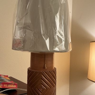 Sale Photo Thumbnail #133: Modern wooden table lamp with a carved geometric chevron base, pull chain, and light gray shade wrapped in original protective plastic.