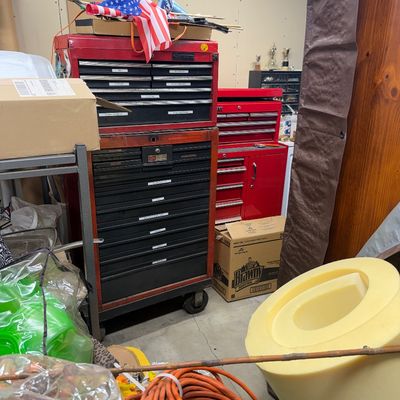 Red metal rolling tool chests surrounded by various workshop items, including an orange extension cord and foam padding.