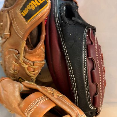 Collection of used leather baseball and softball gloves, including a tan Wilson model, showing moderate wear and lacing detail.