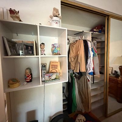 White cube shelving unit filled with novelty items, photo frames, and collectibles alongside an open closet area with hanging clothing.