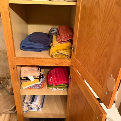 Sale Photo Thumbnail #111: Tall oak linen cabinet filled with various bath towels, hand towels, washcloths, and paper products.