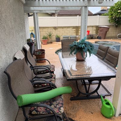 Outdoor patio dining set featuring a large tile-top table, matching high-back metal armchairs with floral seat cushions, and additional...