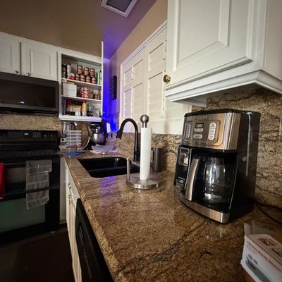 Cuisinart programmable coffee maker set on a granite countertop alongside small kitchen appliances and white cabinetry.