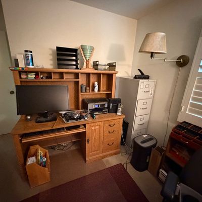 Oak computer desk with upper hutch, accompanied by a computer monitor, printer, metal filing cabinet, paper shredder, and brass swing-arm...