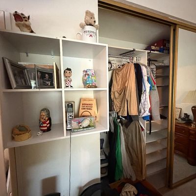 White organizer unit with assorted collectibles and decor, alongside a bedroom closet filled with hanging clothes.