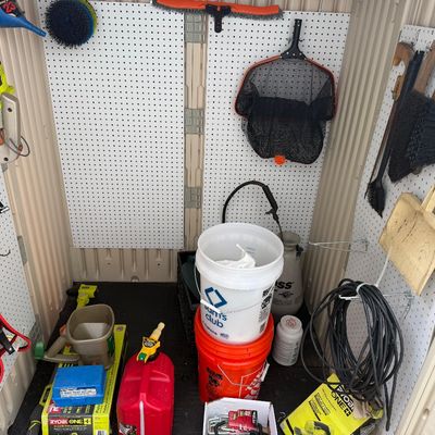 An assortment of lawn care items, power tools, and outdoor supplies arranged inside a plastic storage shed with pegboard walls.