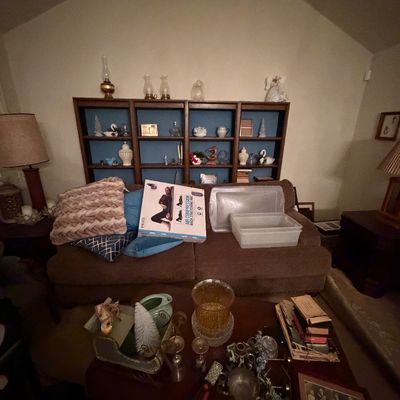 Living room setup featuring a brown upholstered sofa, large dark wood bookcase unit filled with decorative glassware and trinkets, and a...
