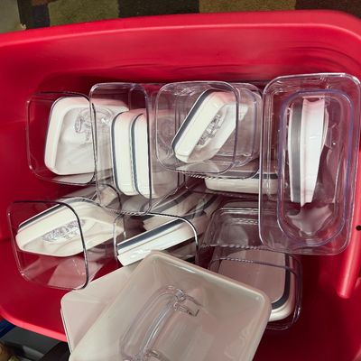 Large red plastic storage tote filled with modern clear acrylic OXO-style airtight food storage containers with white lids.
