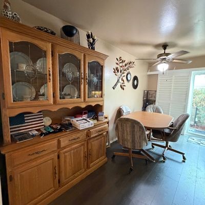 Large light oak china cabinet hutch alongside a matching wooden dining table with upholstered swivel rolling chairs.