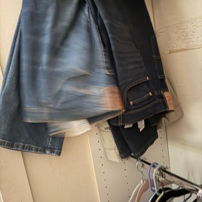 Sale Photo Thumbnail #112: Two pairs of men's dark-wash denim jeans hanging on closet rack, showing moderate wear.