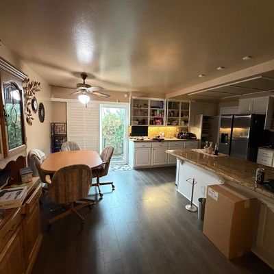Spacious kitchen and dining area featuring a wooden hutch, a casual dining table with upholstered rolling chairs, and an island with...