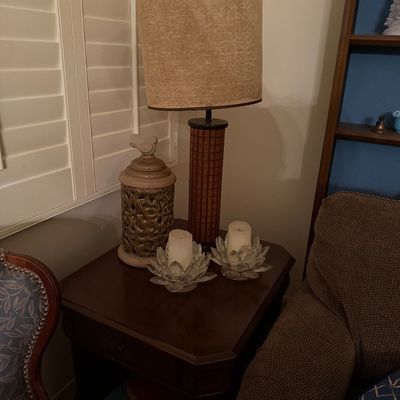 Mid-century style table lamp featuring a textured grid body and tall burlap drum shade, set on a dark wood end table alongside glass...