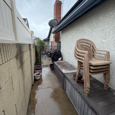 Stack of tan plastic lawn chairs resting on long outdoor storage benches along a side yard walkway.