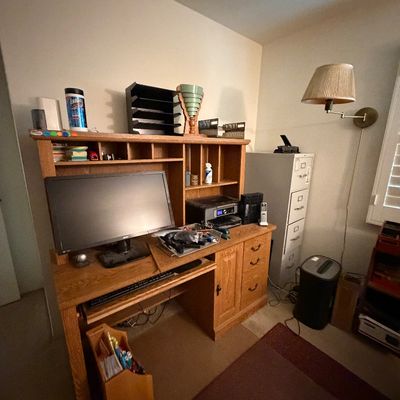 Traditional oak computer desk with hutch, featuring a computer monitor, office supplies, and paired with a four-drawer filing cabinet.