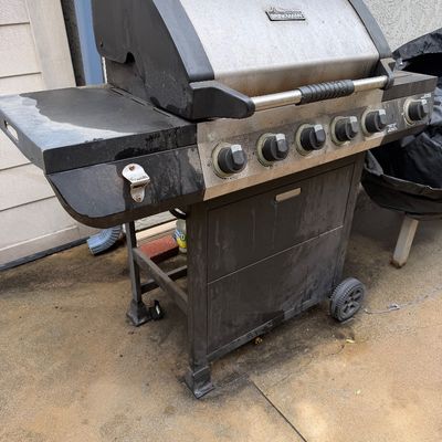 Brinkmann 5-burner gas grill with stainless steel lid, side burner, and attached bottle opener, showing outdoor wear.
