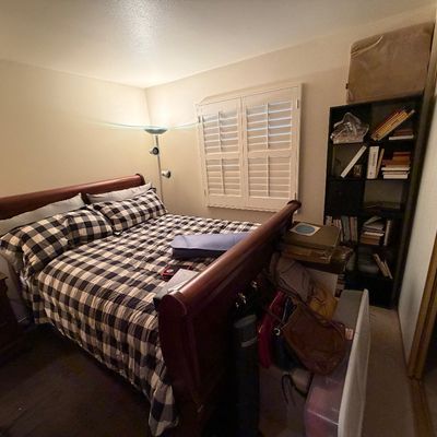 Wooden sleigh bed frame with black and white buffalo check bedding, accompanied by a tall black bookcase and matching nightstand.