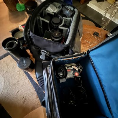 Collection of camera bags containing vintage camera equipment and accessories, including Canon camera lenses, a Vivitar 2600 electronic...