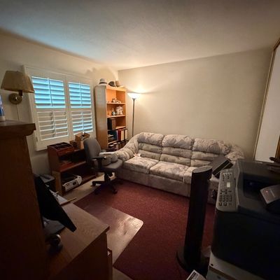 Home office setup featuring a patterned three-cushion reclining sofa, wooden bookshelves, an executive desk, an office chair, and various...