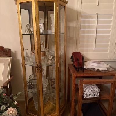Tall octagonal curio cabinet with a gold gilt finish and glass display shelves, filled with cut crystal and decorative glassware.