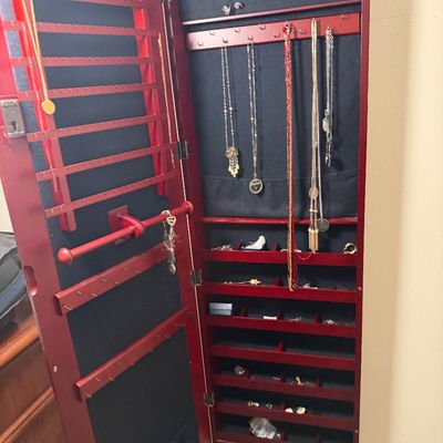 Sale Photo Thumbnail #105: Wall-mounted cherry-finish jewelry armoire with black felt lining, filled with various necklaces, rings, and accessories.