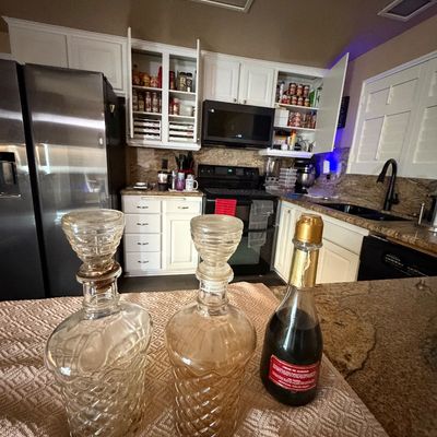 Pair of vintage diamond-pattern pressed glass decanters with stoppers displayed alongside a bottle of Creme de Almond liqueur.